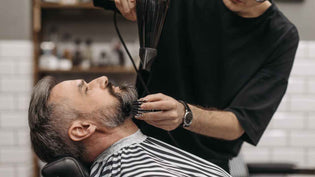  Man leaning back in barbershop while barber blowdries beard | Style Standard